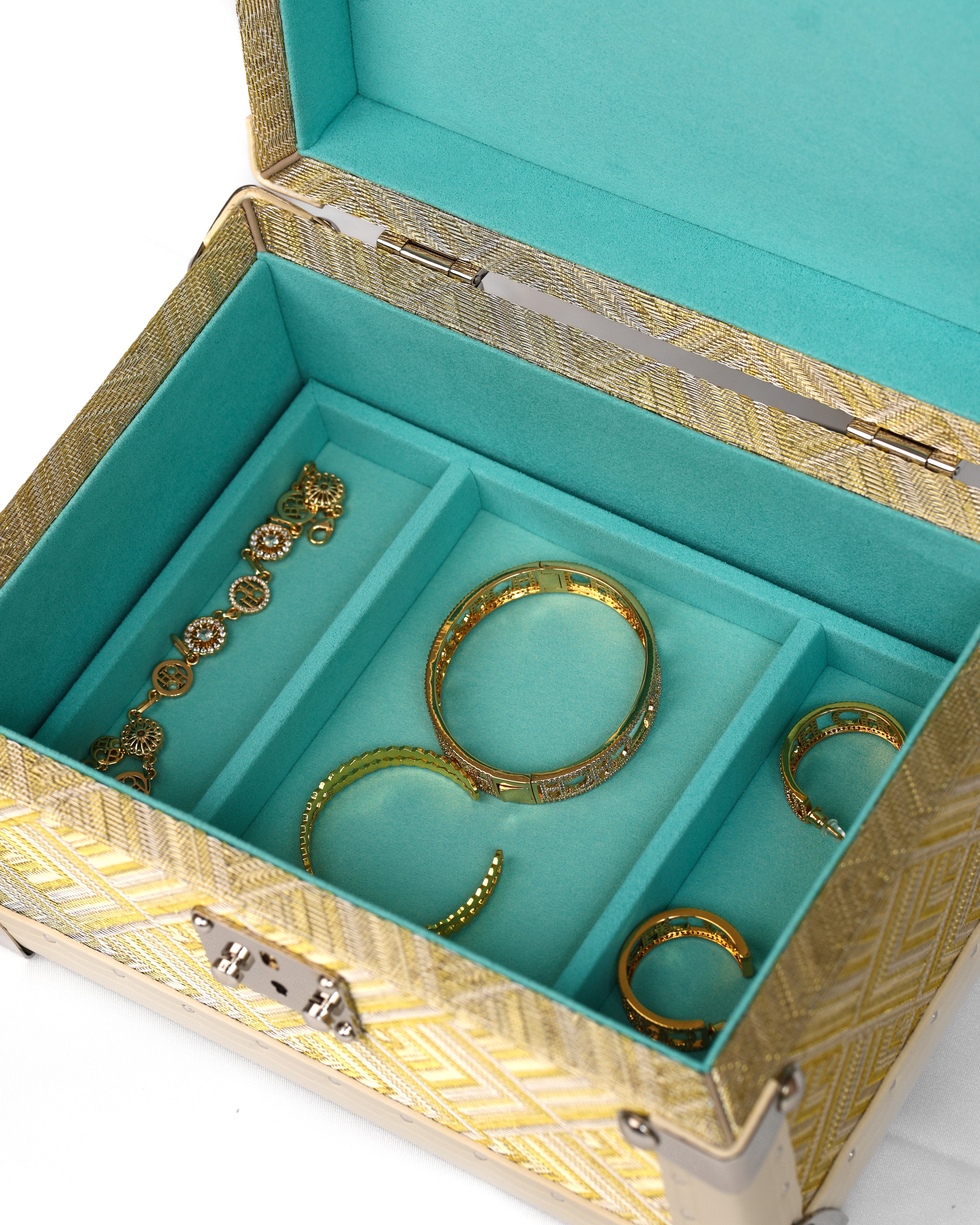 An open jewelry box with a turquoise velvet interior and a gold patterned exterior, holding several gold-toned bangles and rings.