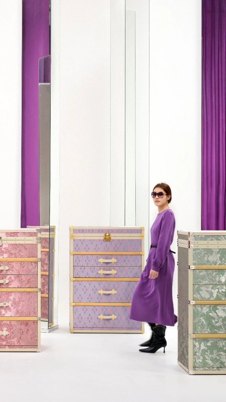 Woman standing among colorful storage drawers with purple curtains in the background